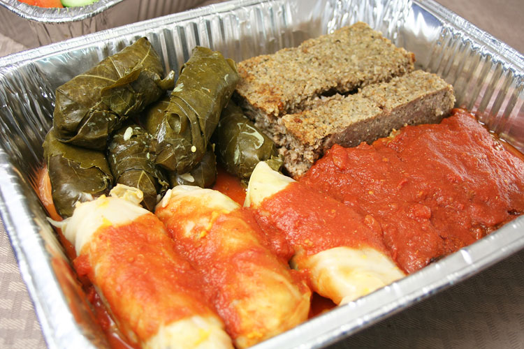 Catering tray with rolled grape leaves, baked kibbie and rolled cabbage in tomato sauce